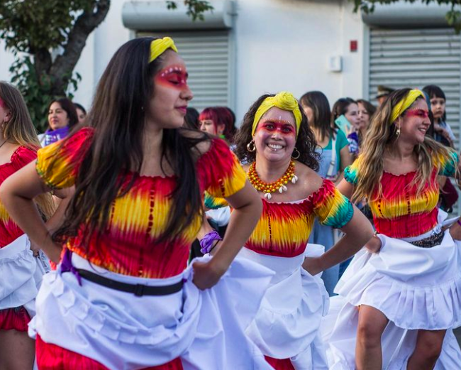 Mujeres marchan vestidas con un vestido naranjo amarillo y blanco en la marcha de chillán