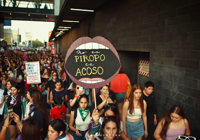 Dentro de un grupo de mujeres una sostiene un cartel en forma de boca que dice "No es piropo, es acoso"